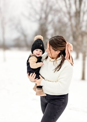 Winter photoshoot of a parent and child playing in the snow wearing warm clothing.