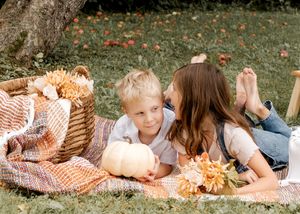 Family lying on picnic blanket together in autumn garden setting.
