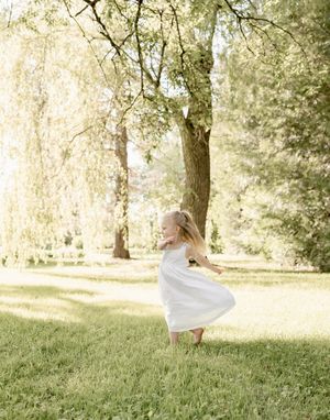 A whimsical twirl in a white dress captured in golden sunlit parkland.