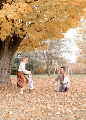 A playful autumn scene with people enjoying the fallen leaves under golden trees.