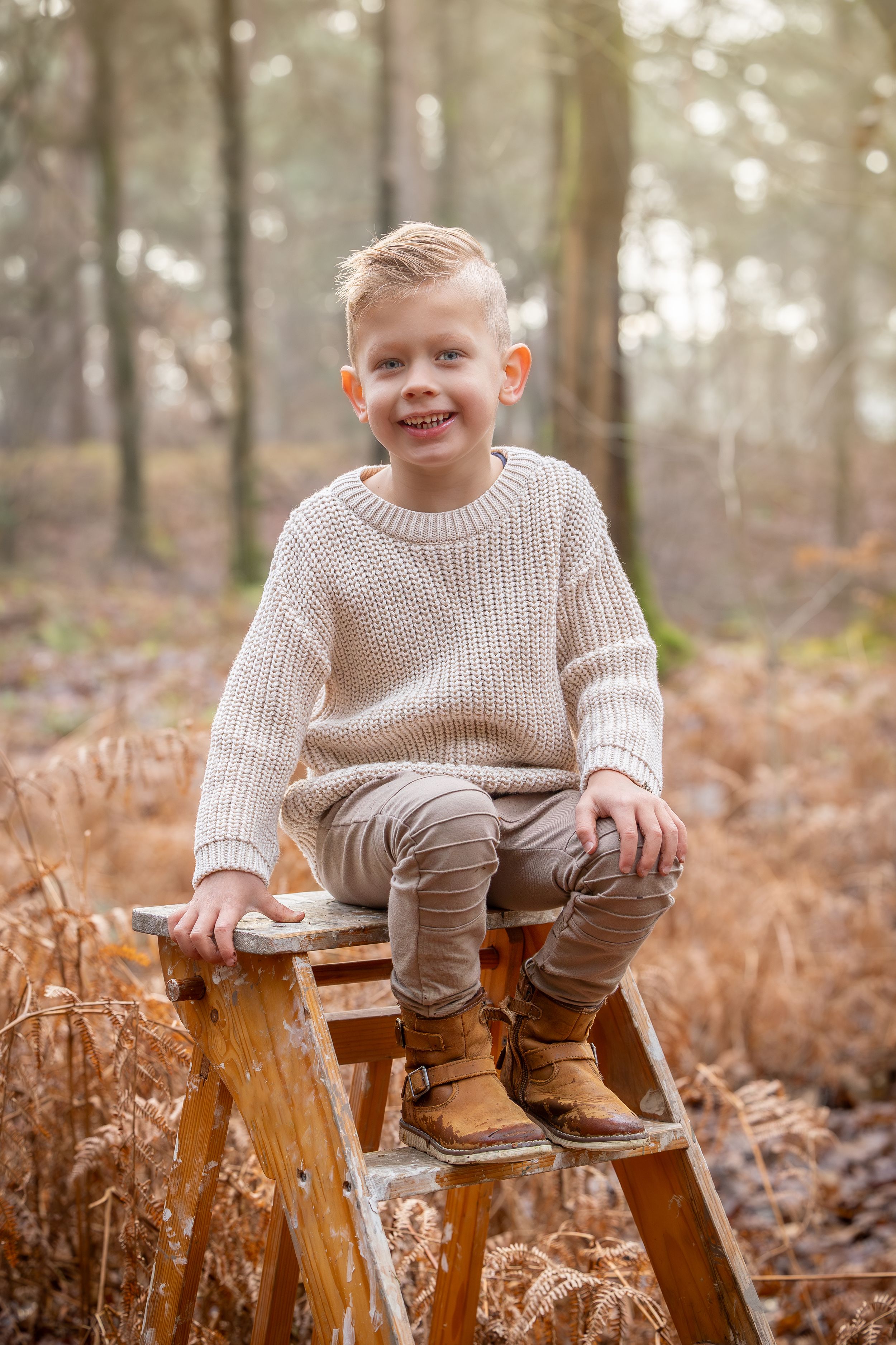lachend jongetje op houten trapje tijdens een fotosessie in de natuur