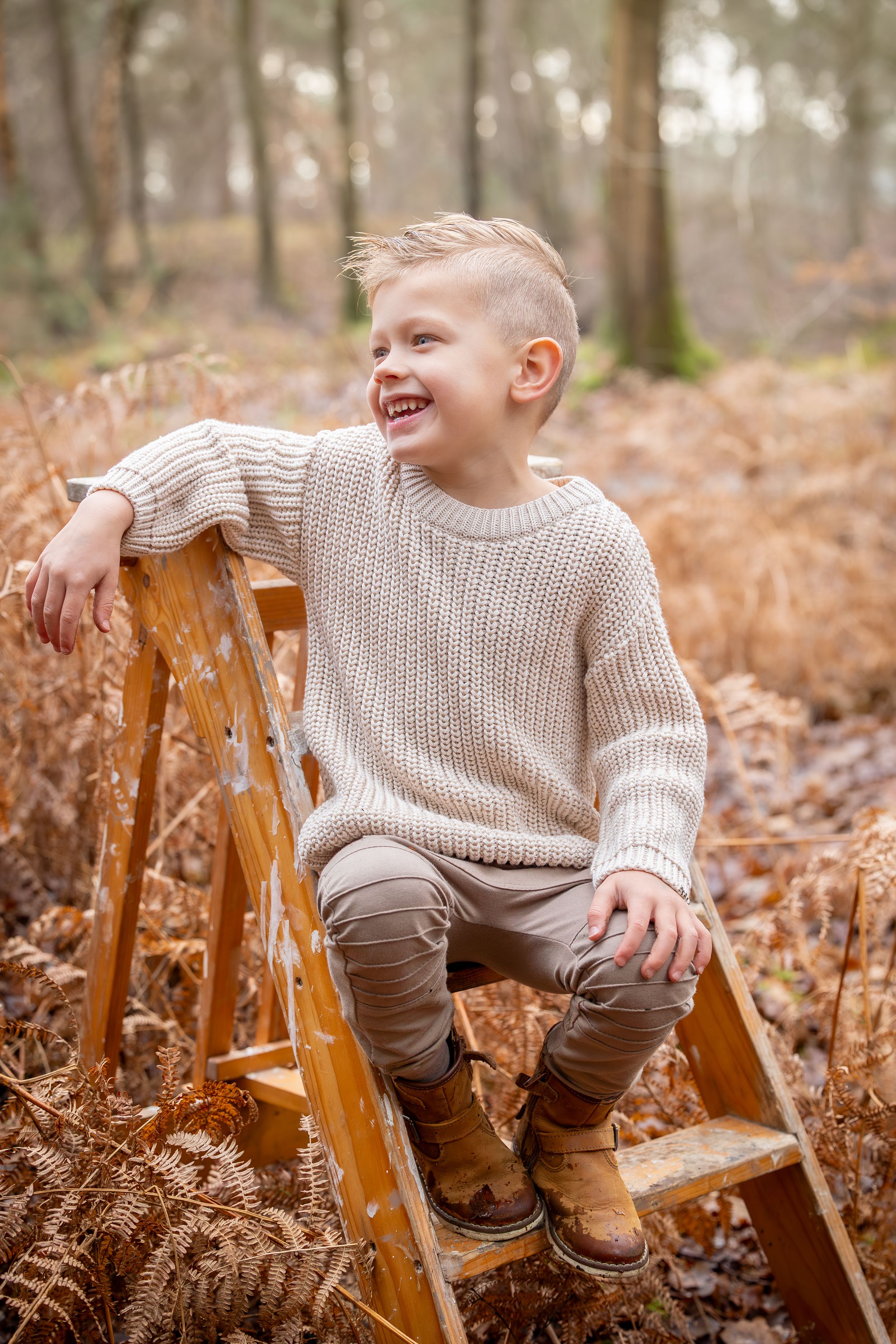 jongetje op houten trap. gekleed in creme / bruintinten tijdens een fotoshoot in de natuur