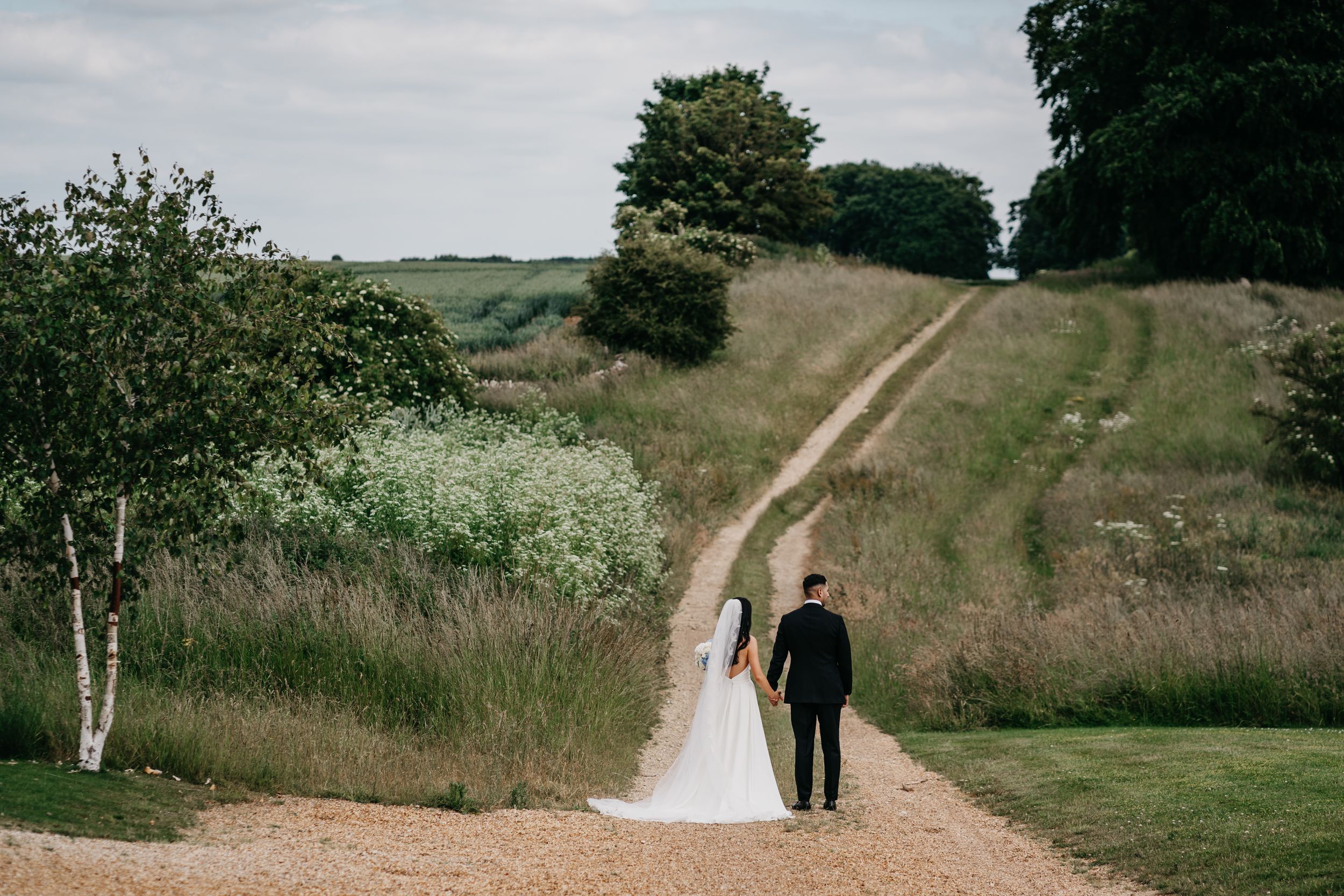 A scenic dirt path winds through rolling green hills with trees dotted along the countryside.