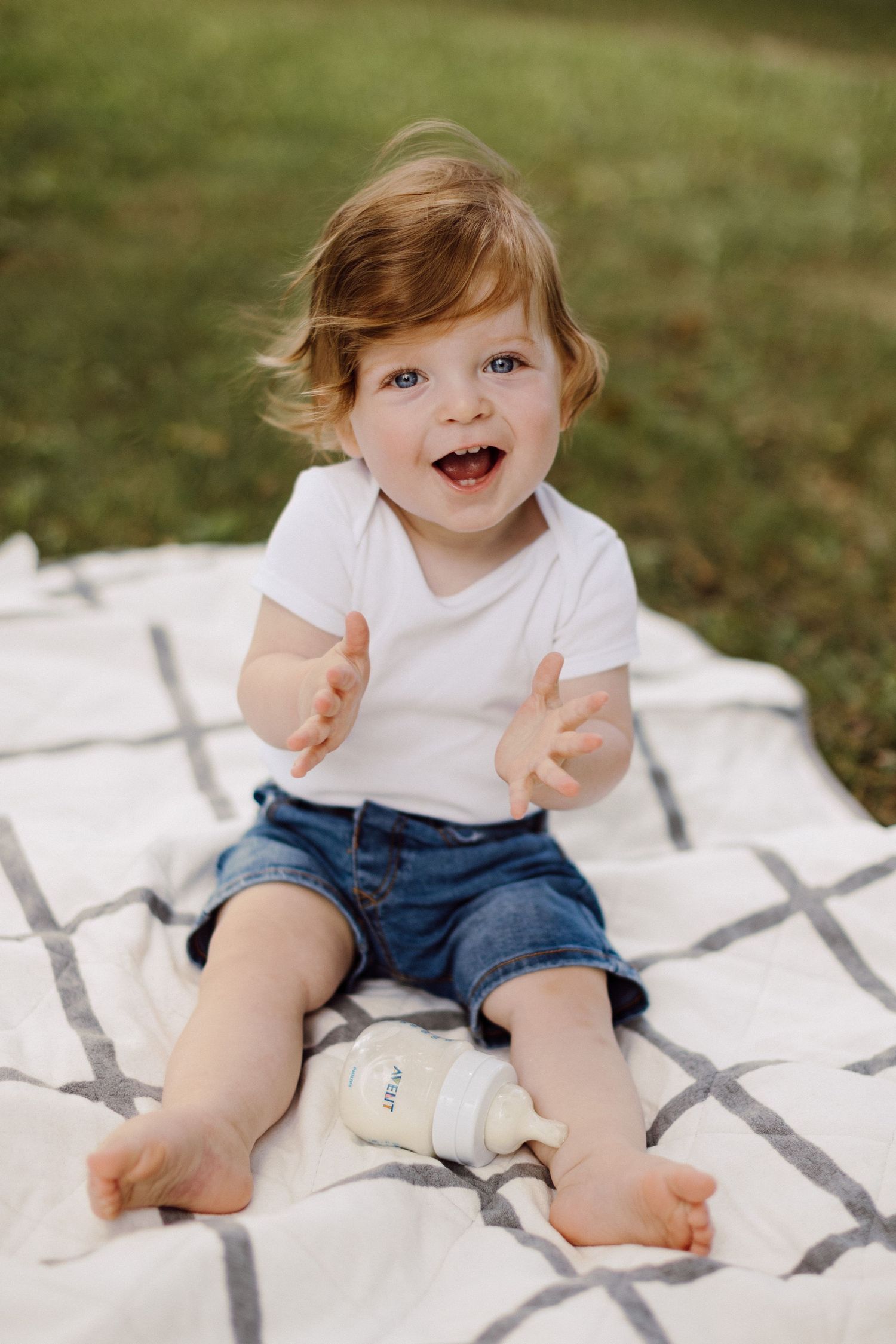 Happy toddler sitting on patterned blanket outdoors clapping hands.
