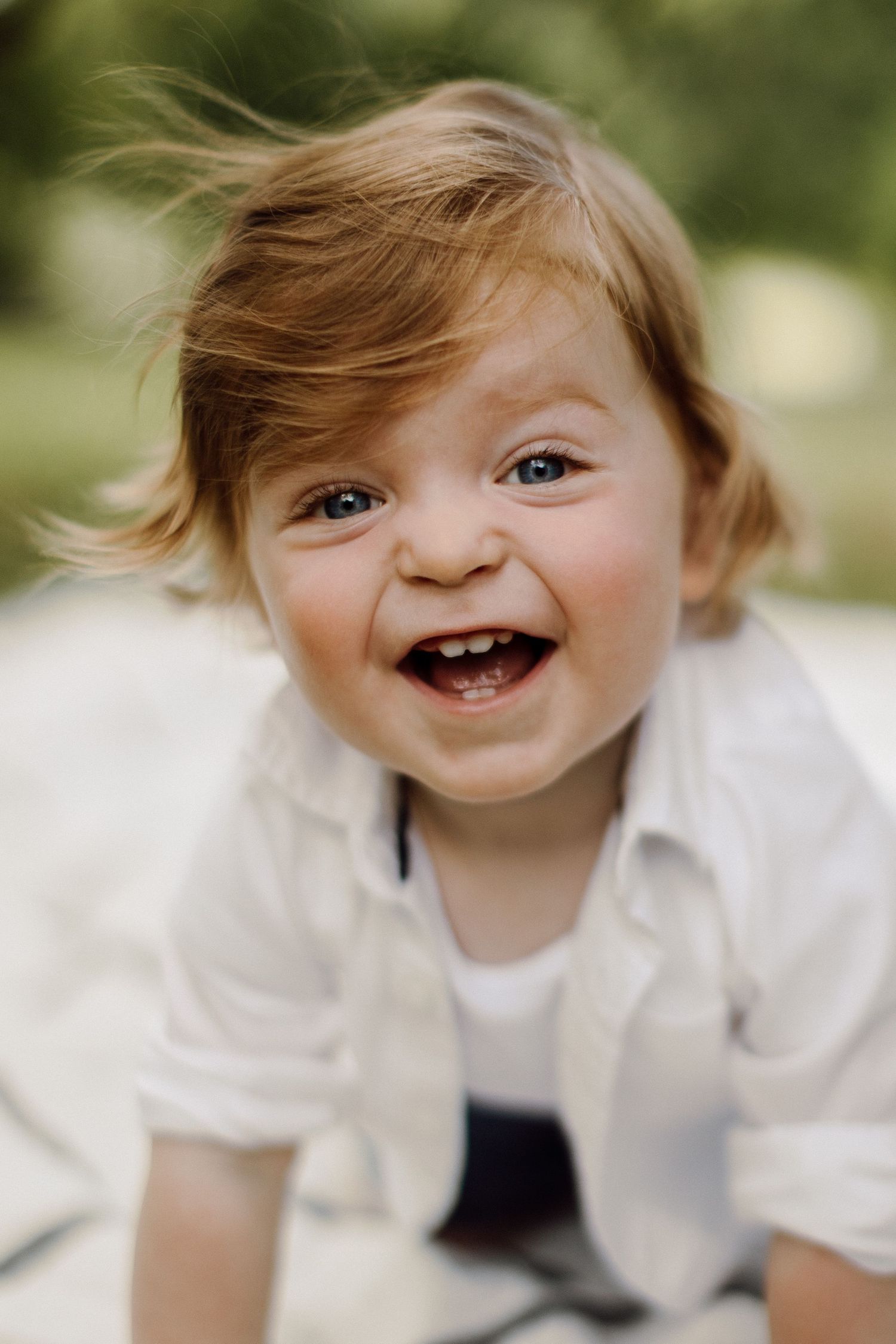 Joyful toddler laughing while wearing white shirt during outdoor photoshoot.