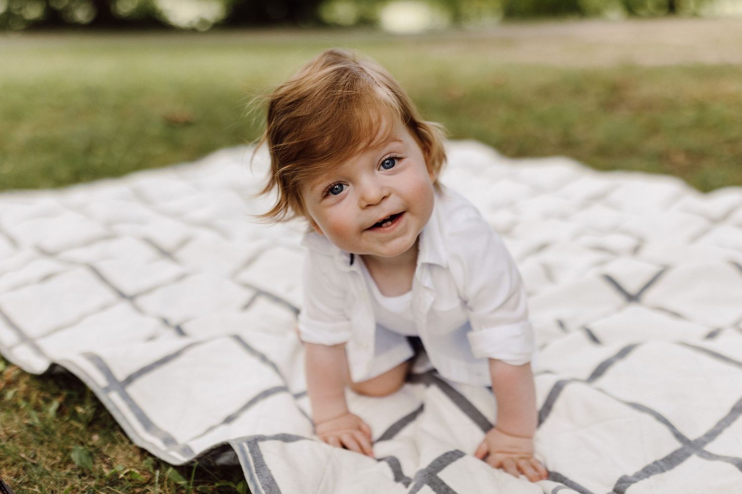 Family enjoying playful moments together on a patterned outdoor patio in casual white outfits.