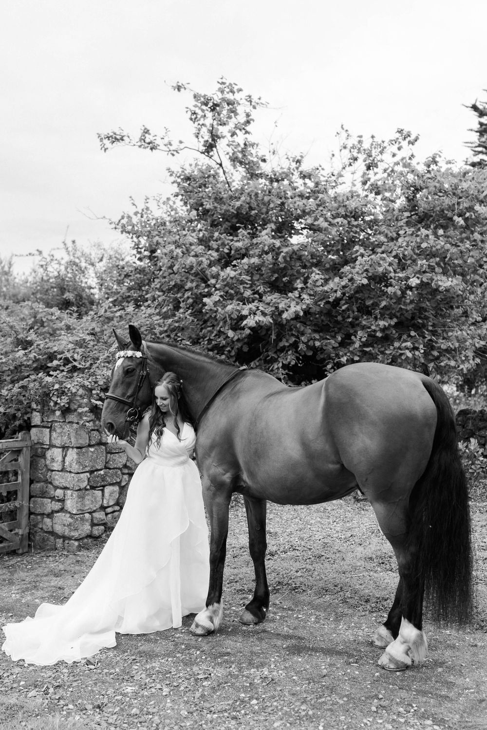 A series of black and white photos showing a person in a white dress standing next to a dark horse against a stone wall.