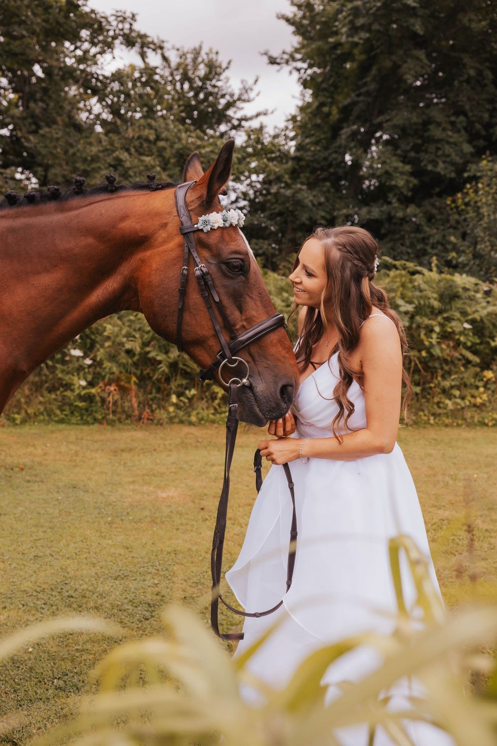 A beautiful chestnut horse and rider in a white dress share a tender moment in a sunny meadow.