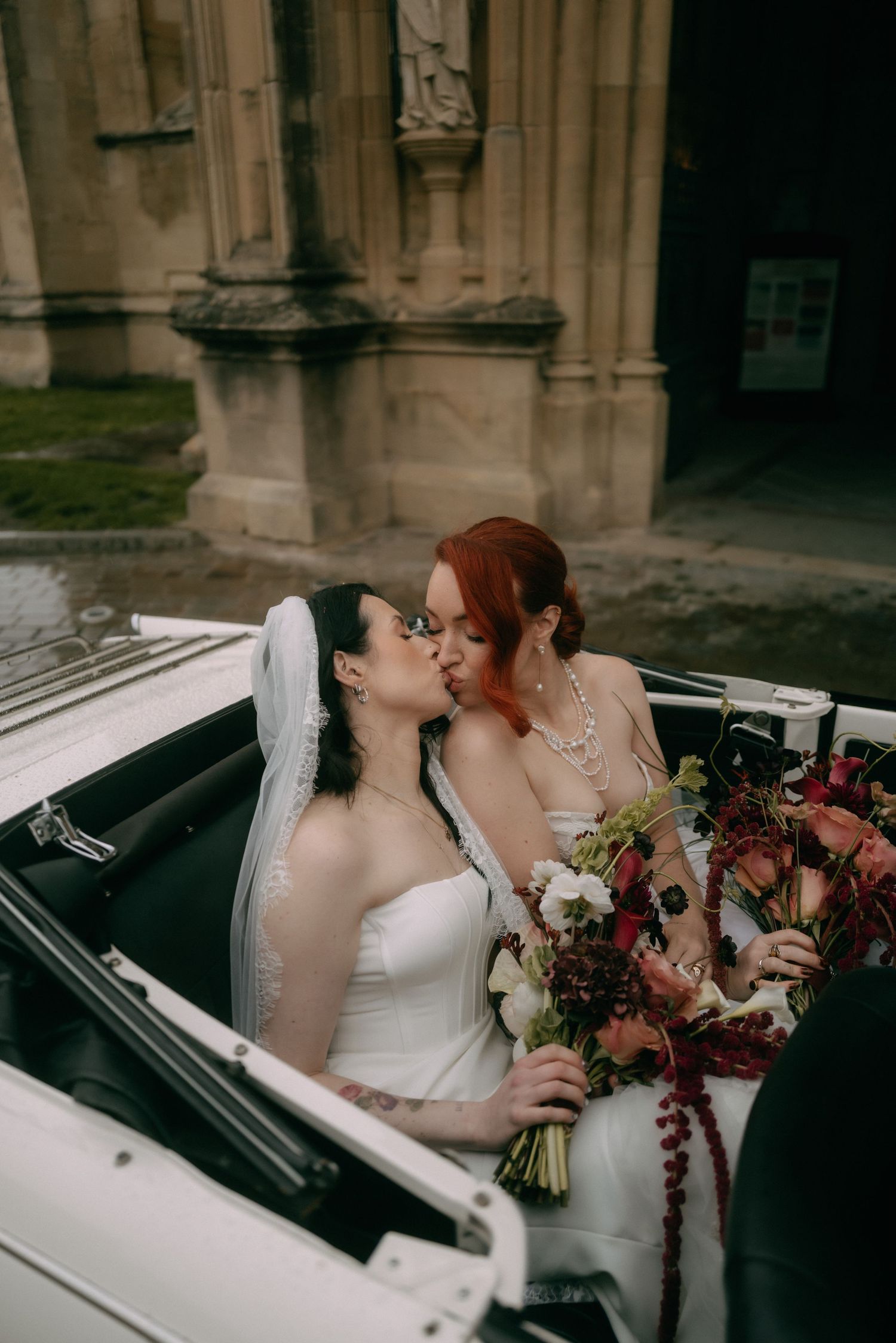 A romantic couple sharing intimate moments in a classic white car outside a historic stone building.