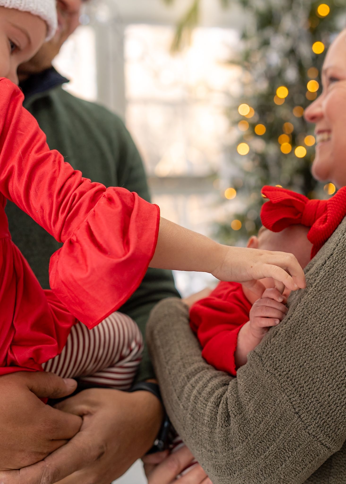 Intimate family moment captured indoors with twinkling holiday lights in background.