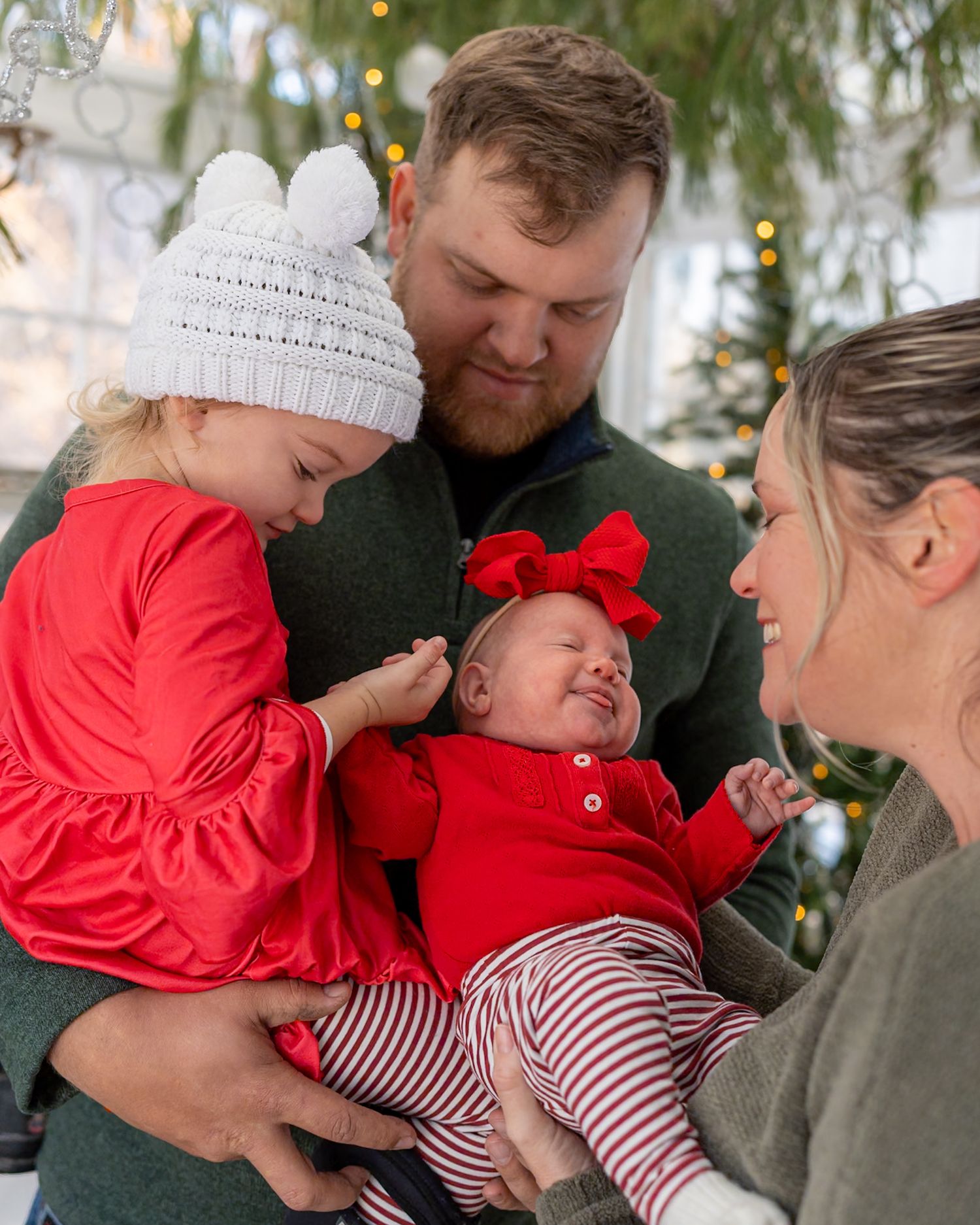 Festive holiday family moment with red and white striped clothing and white knit hat against Christmas decorations.