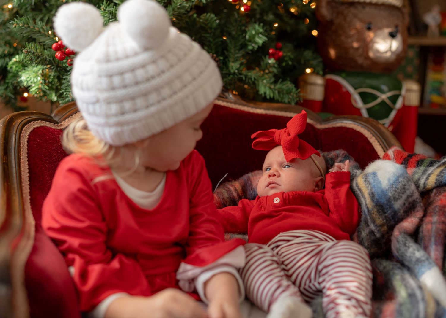 Cozy Christmas scene with white knit hats and red clothing against decorated evergreen tree.