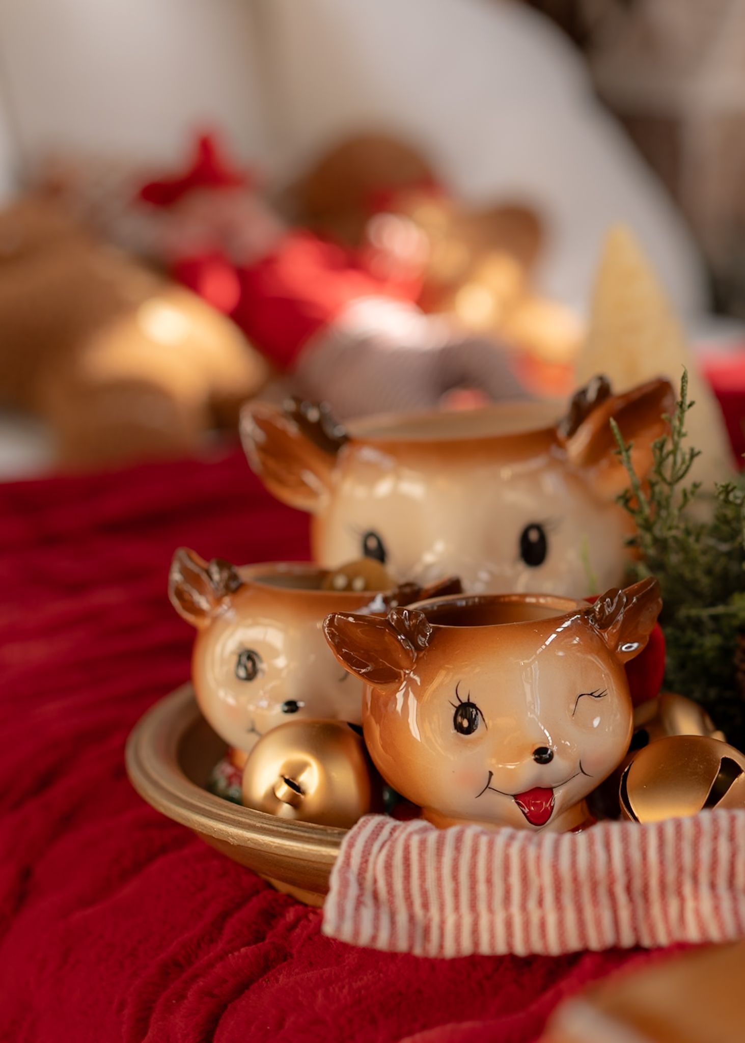 Decorative ceramic reindeer ornaments with red and white striped accents on red fabric.