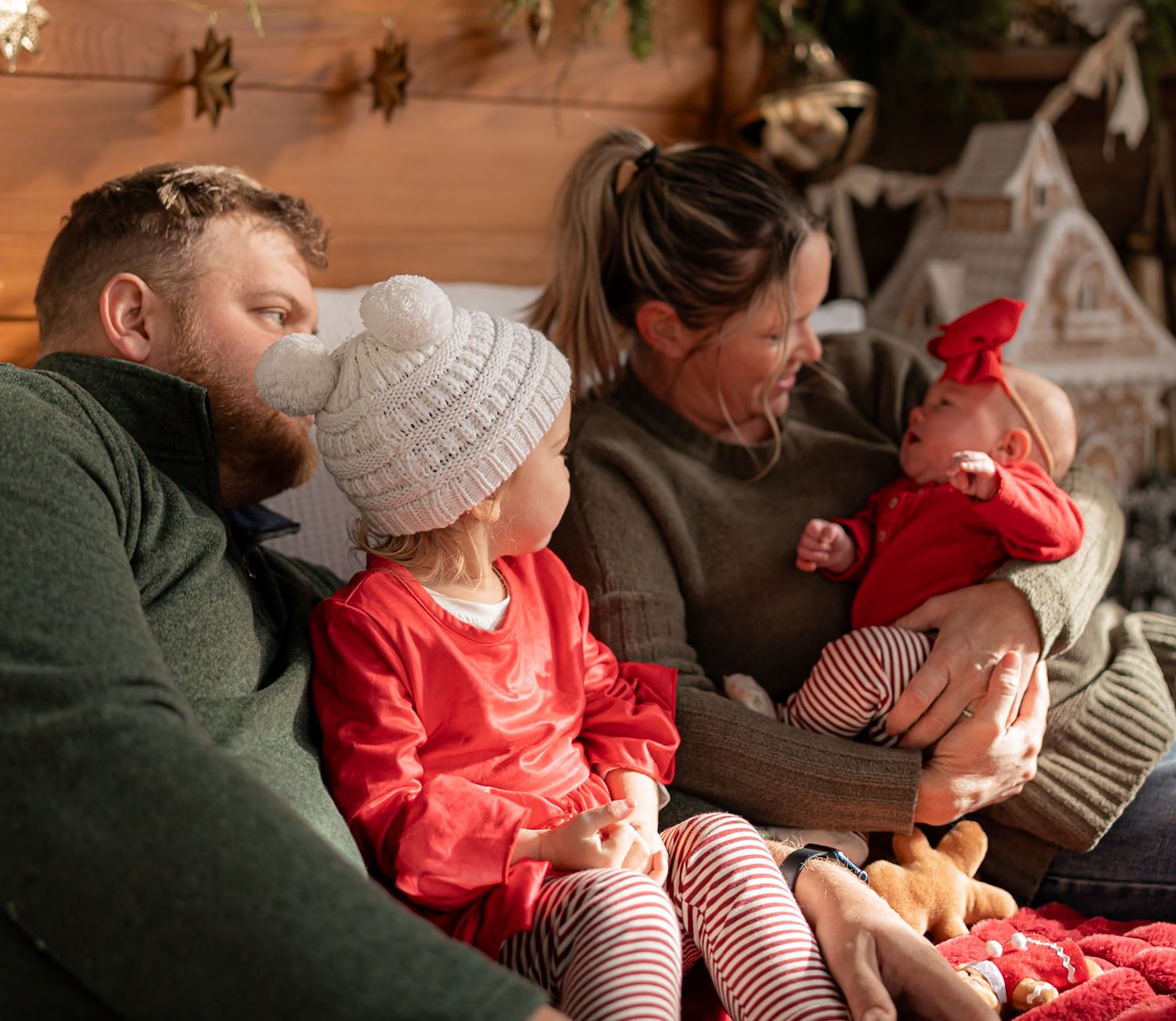 A family relaxes together on a couch during the holiday season wearing festive red and white striped clothing.