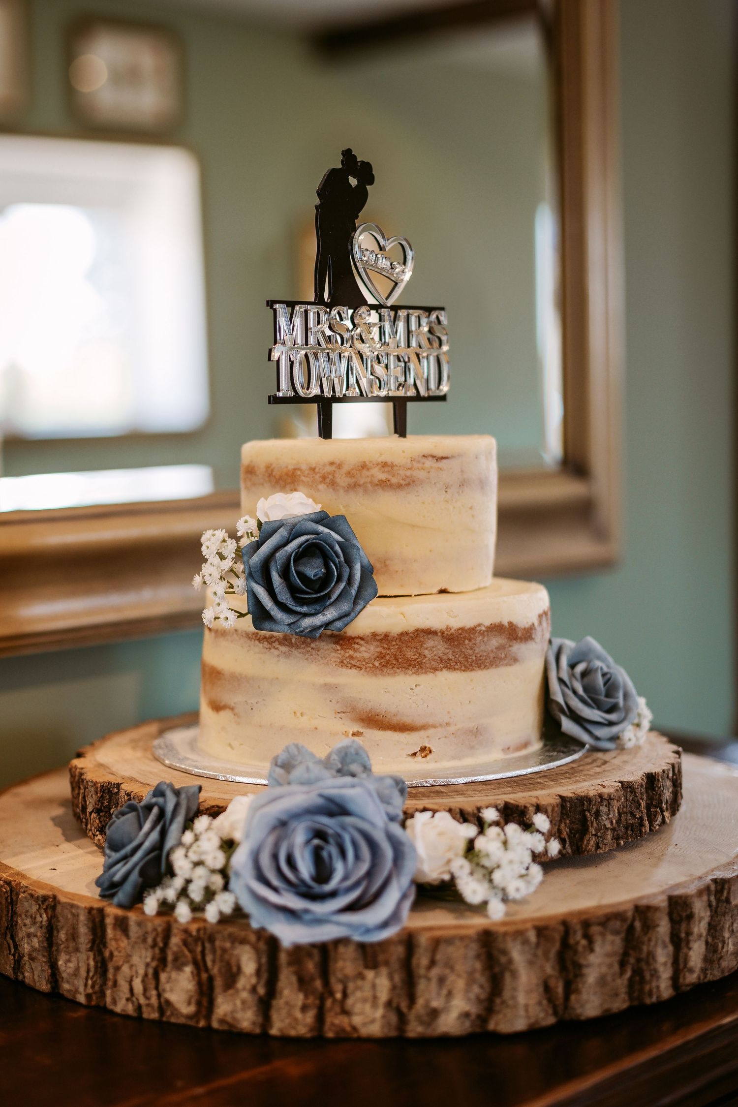 Rustic wedding cake with blue roses displayed on wooden log slices with custom cake topper.