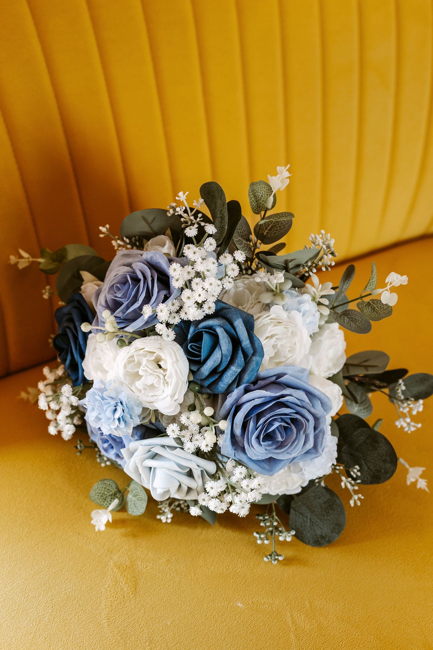 Elegant blue and white floral hair accessories with roses and baby's breath arranged on a yellow background.