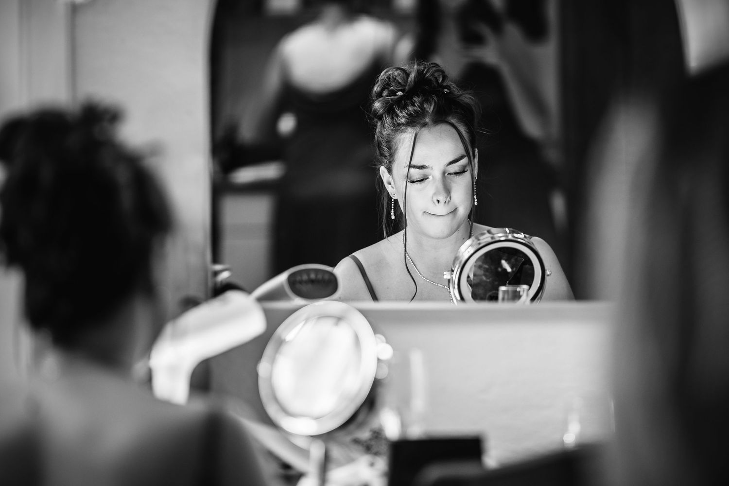 Black and white photo showing bridal preparations with soft window light in elegant getting ready room.