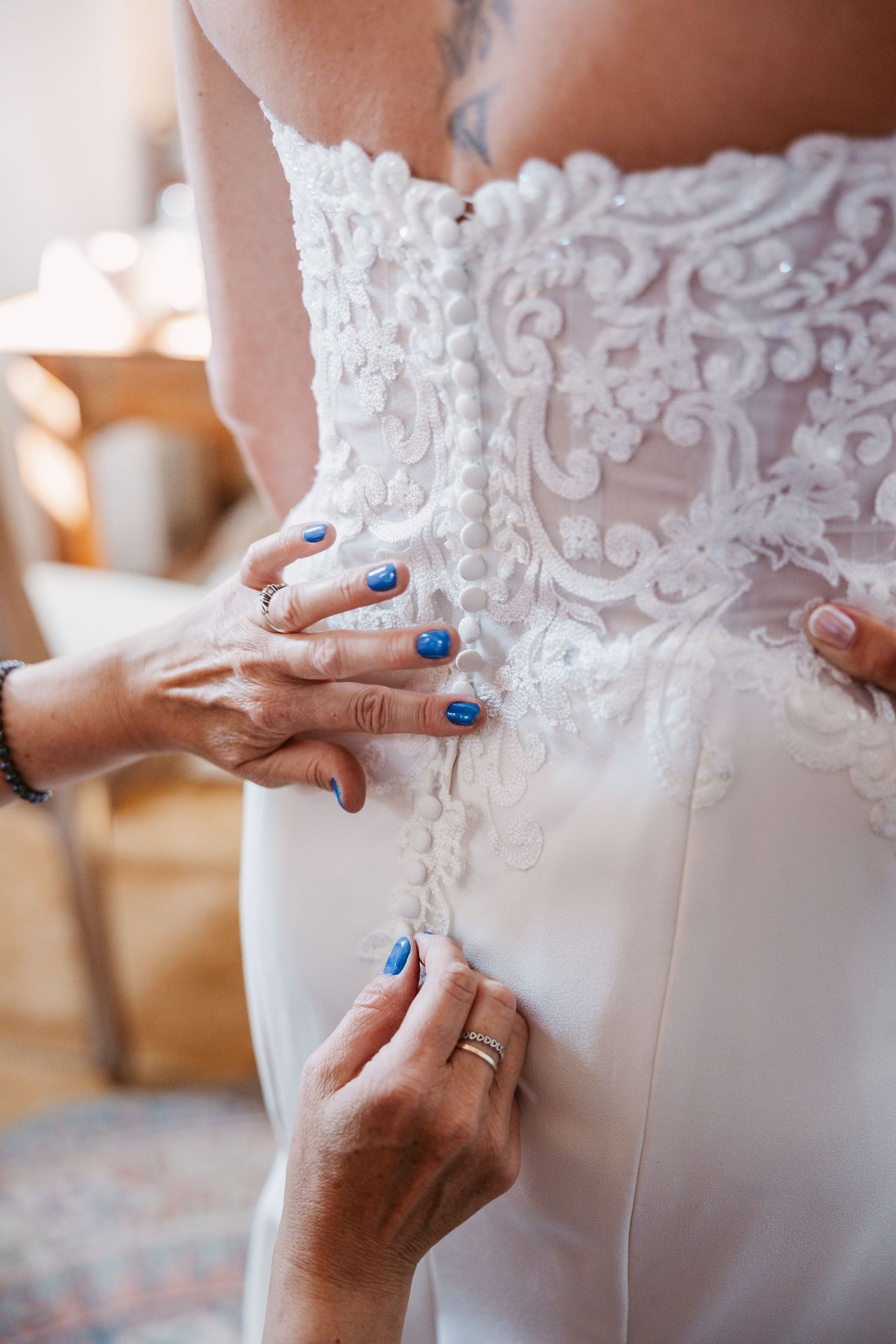 Close-up details of intricate lace and buttons on white wedding dress being fastened.