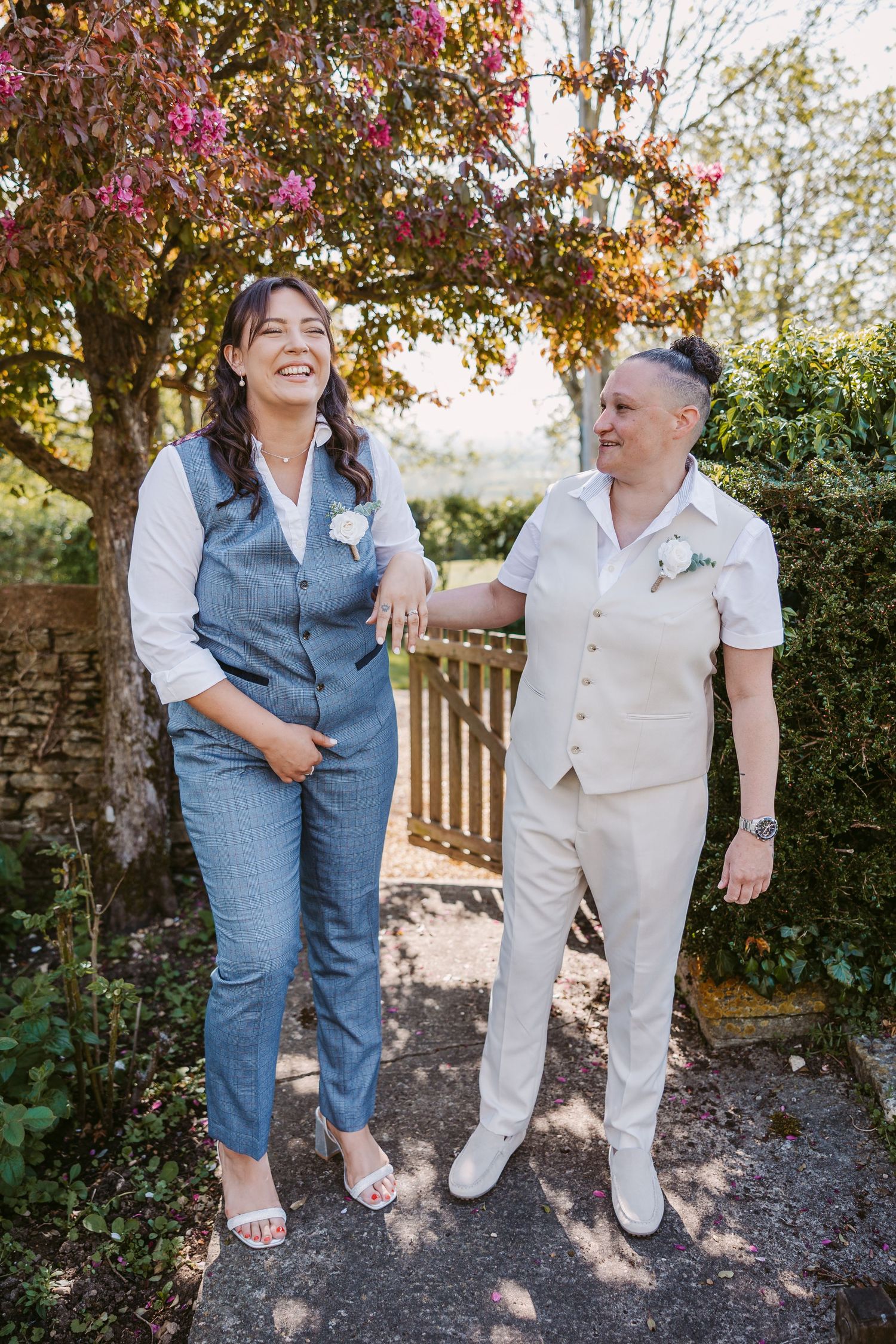 Two people in coordinating outfits walking together in a garden setting with blooming flowers during golden hour.
