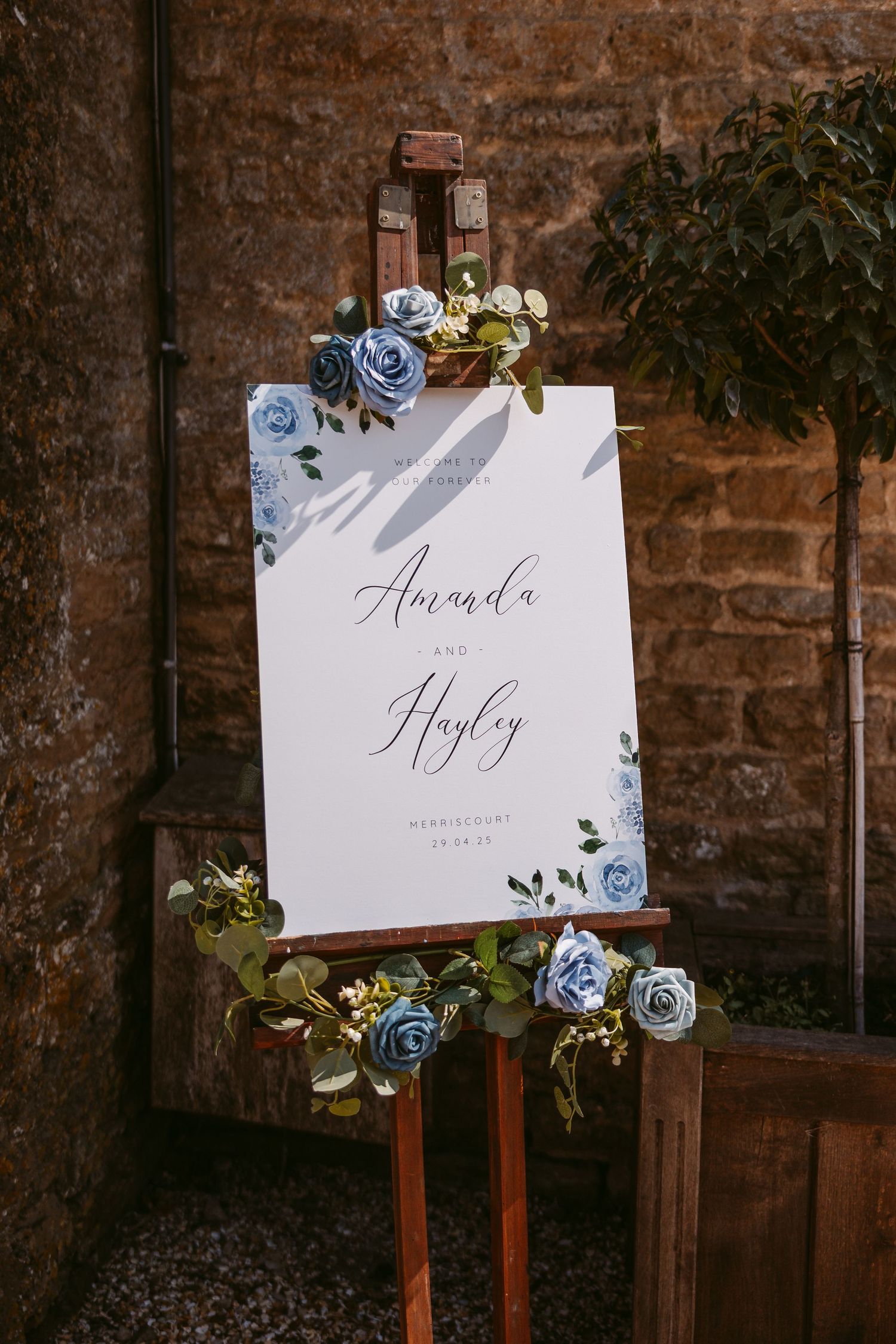 Wedding signage with blue floral decorations displayed against brick wall.