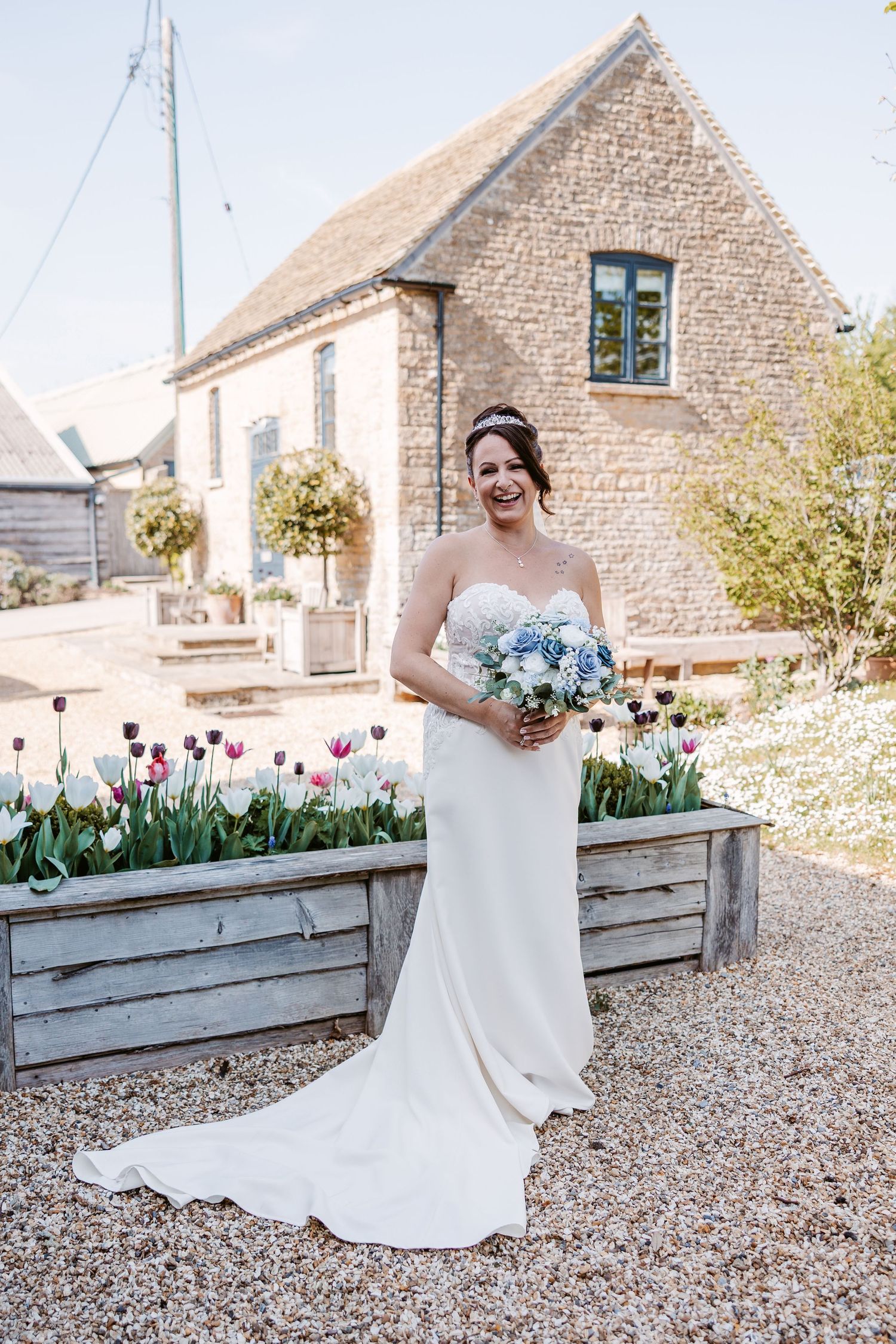 Bride in white dress poses by stone building with spring tulips in garden boxes.