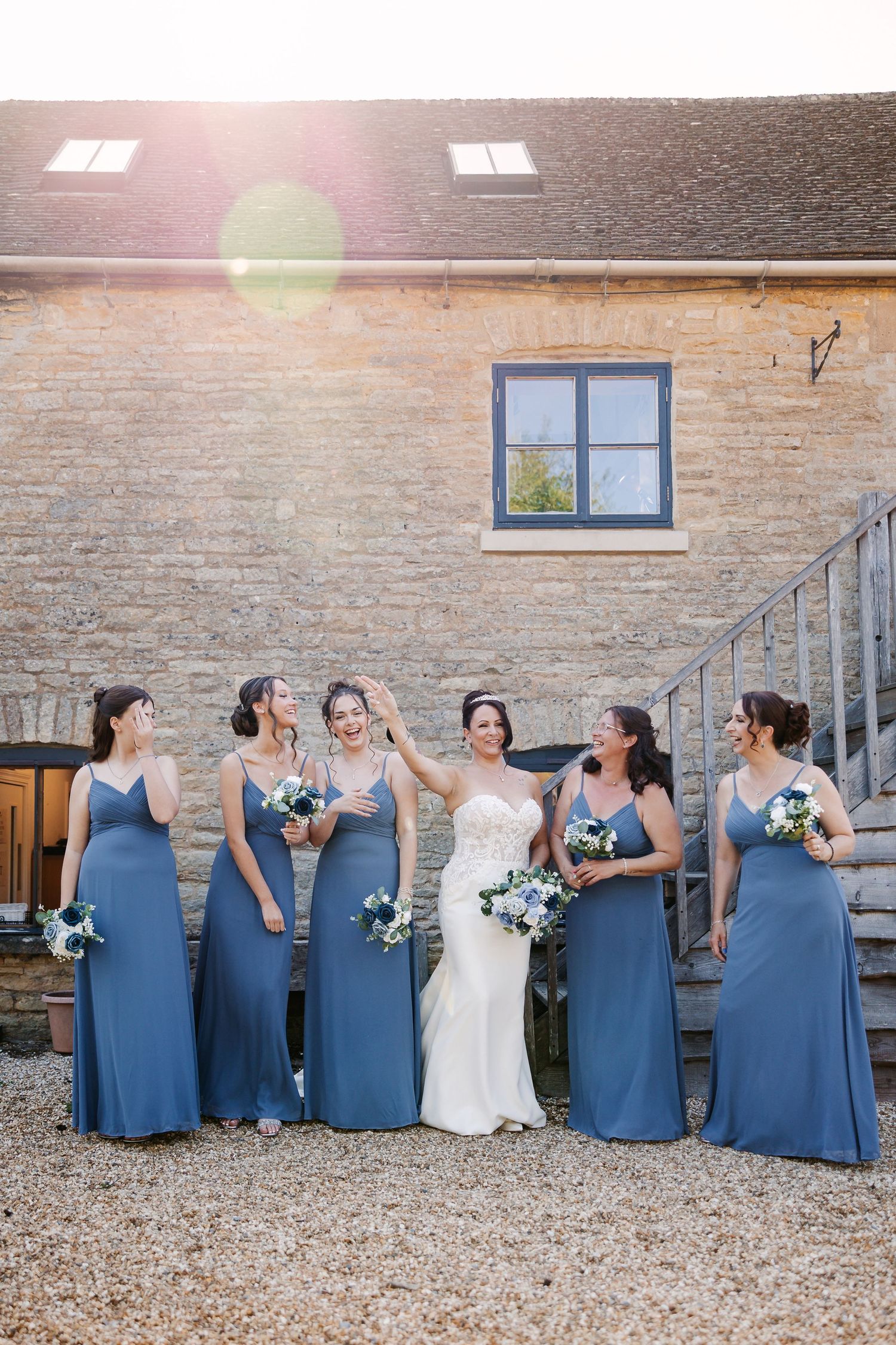Wedding party in white and blue dresses posed against stone building exterior.