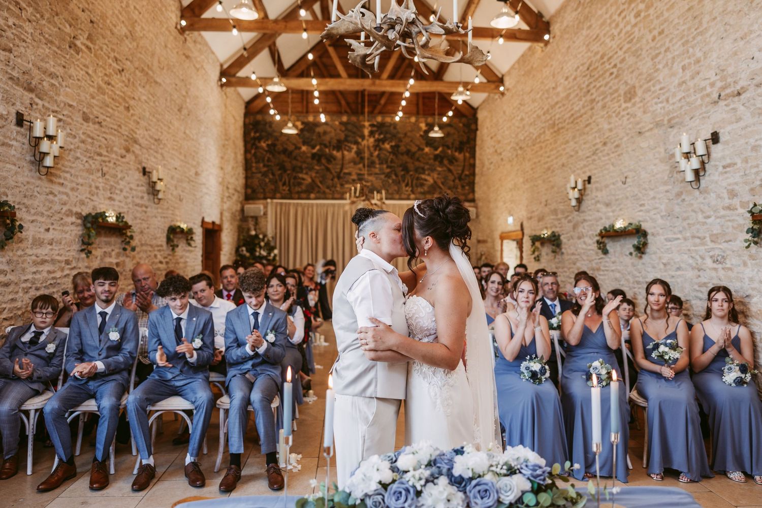 Wedding party in coordinated blue and white attire gathered in rustic barn venue.