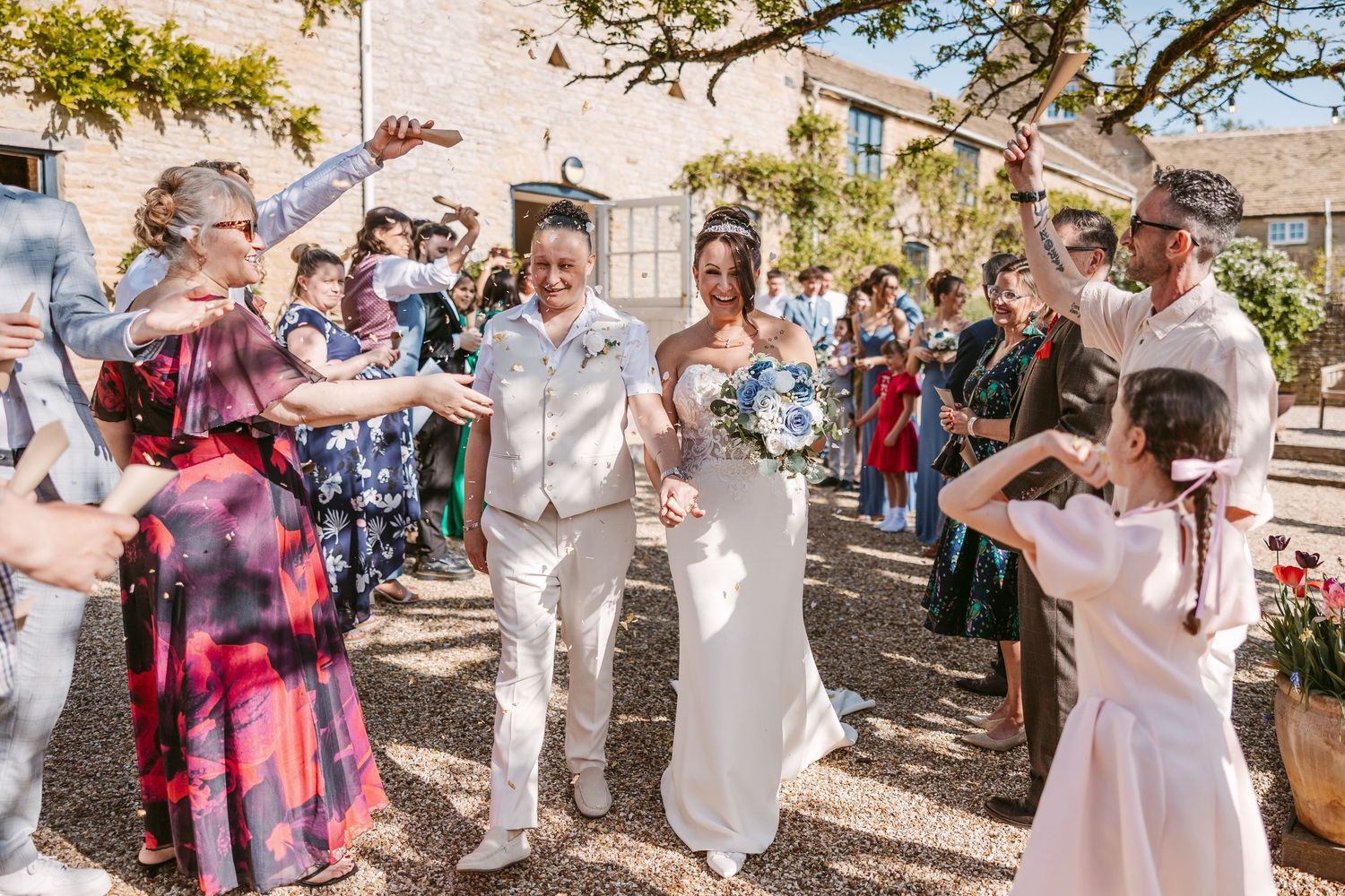 Wedding party celebrates with confetti toss in sunny outdoor garden setting.