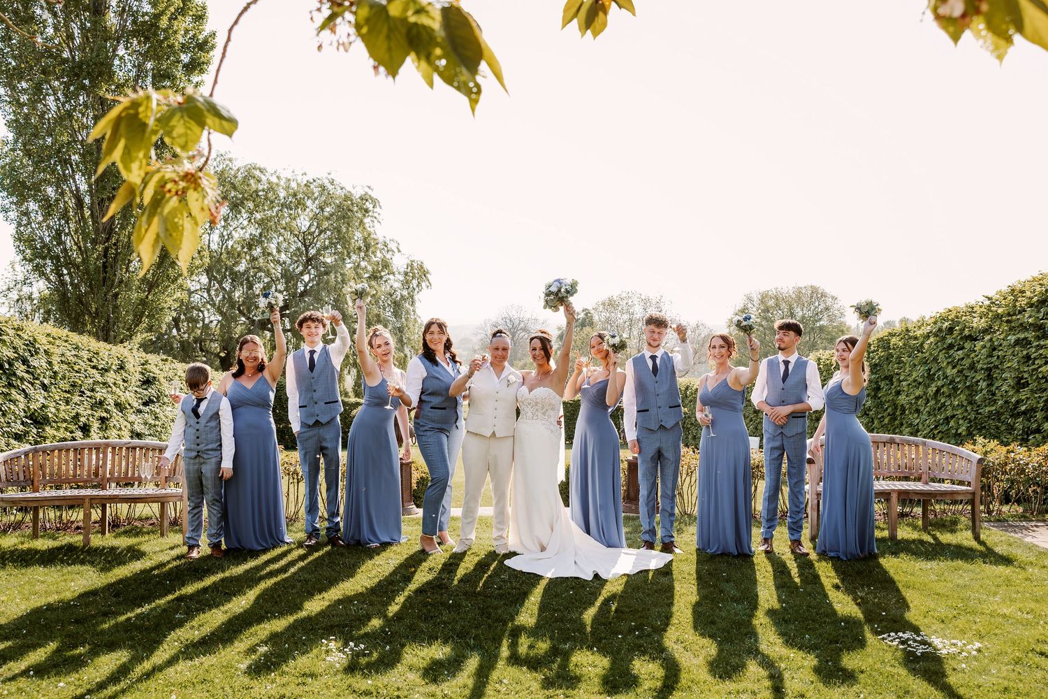 Wedding party in blue and white attire posed for group photos outdoors on a sunny day.