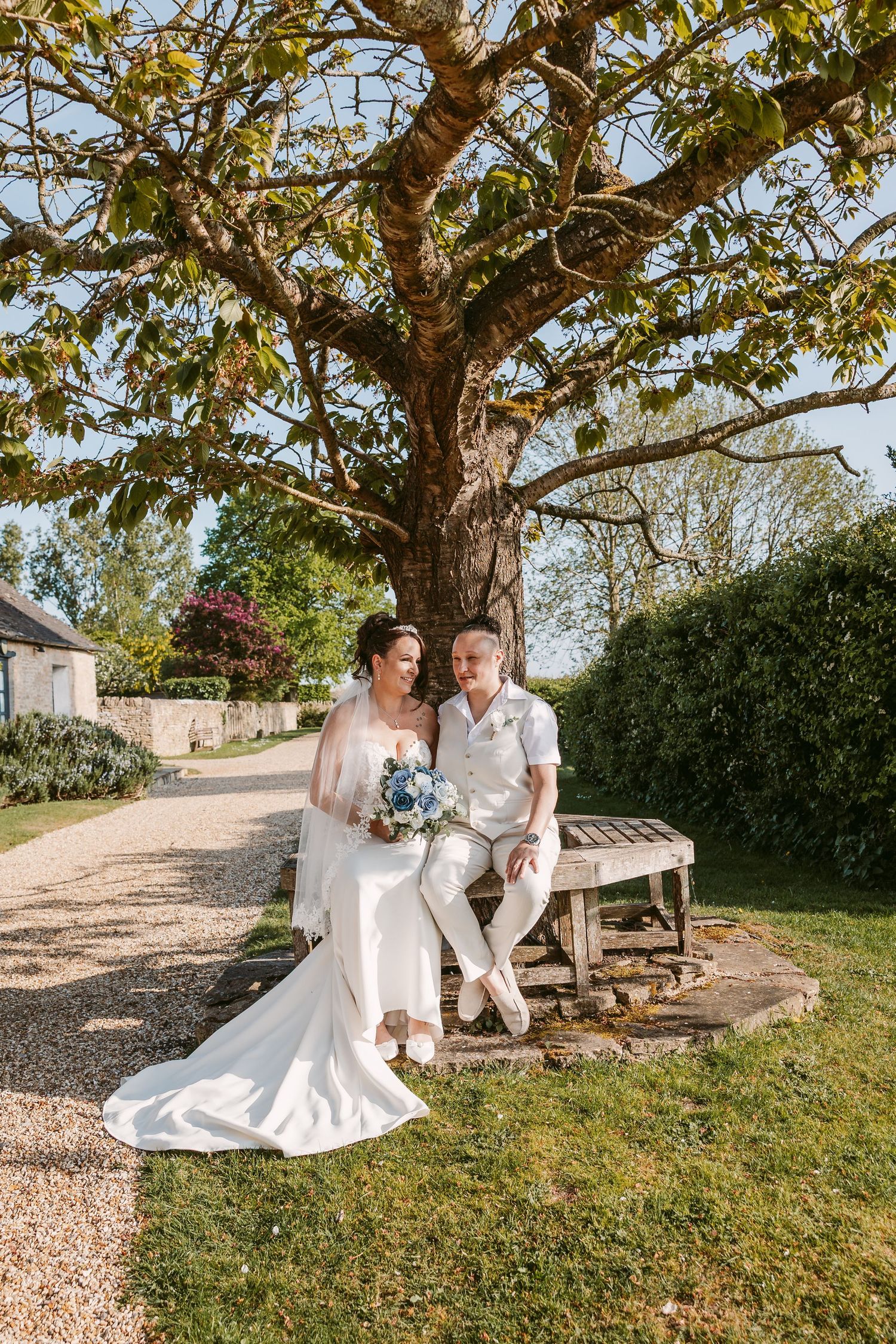 Couple shares romantic moments under large tree on sunny garden grounds.