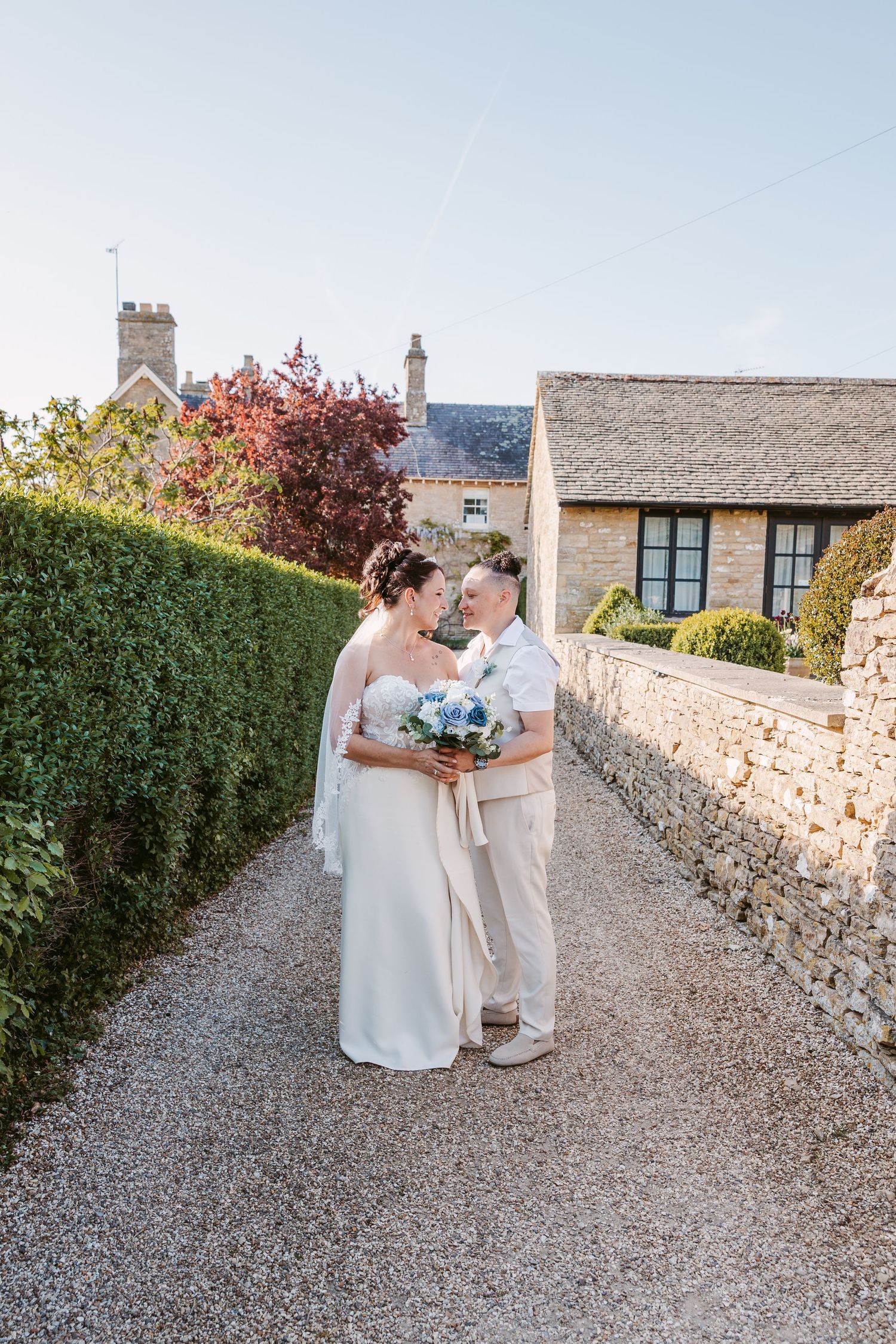 Romantic wedding portraits on a gravel path surrounded by stone walls and gardens.