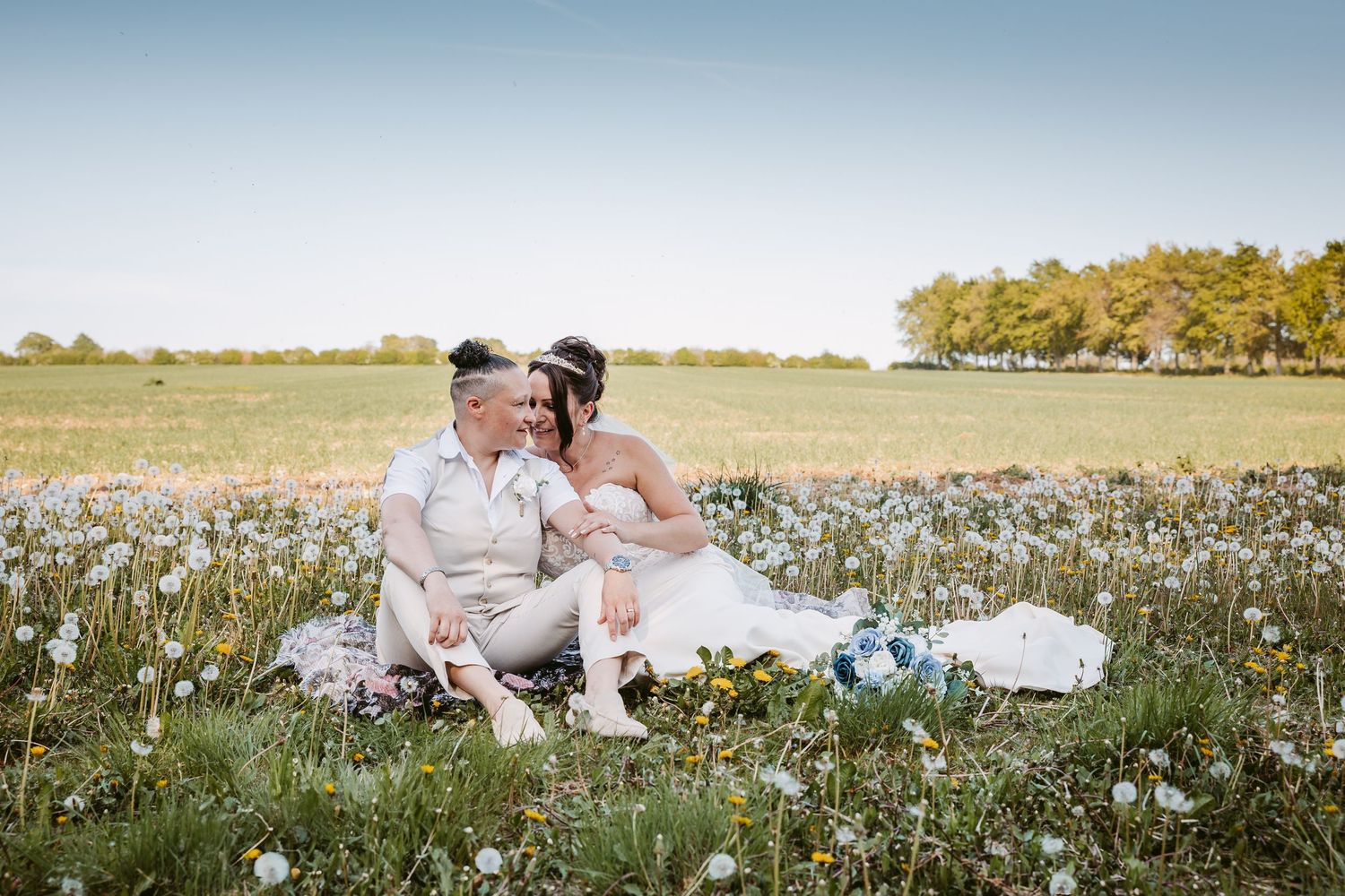 Couple in white sharing intimate moments in a blooming daisy field on their wedding day.
