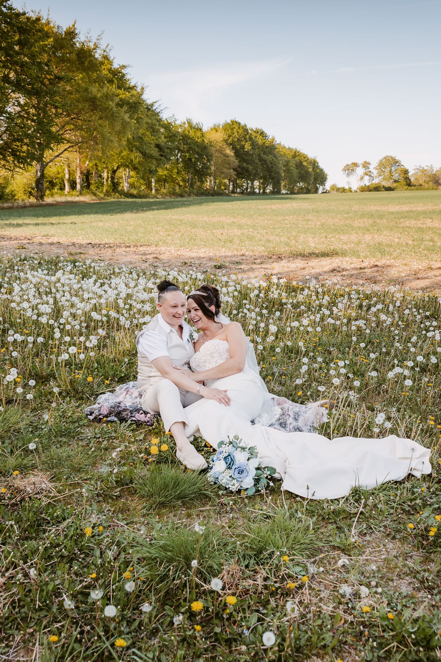 A couple laying in a meadow of white dandelions during a romantic wedding photo session at sunset.