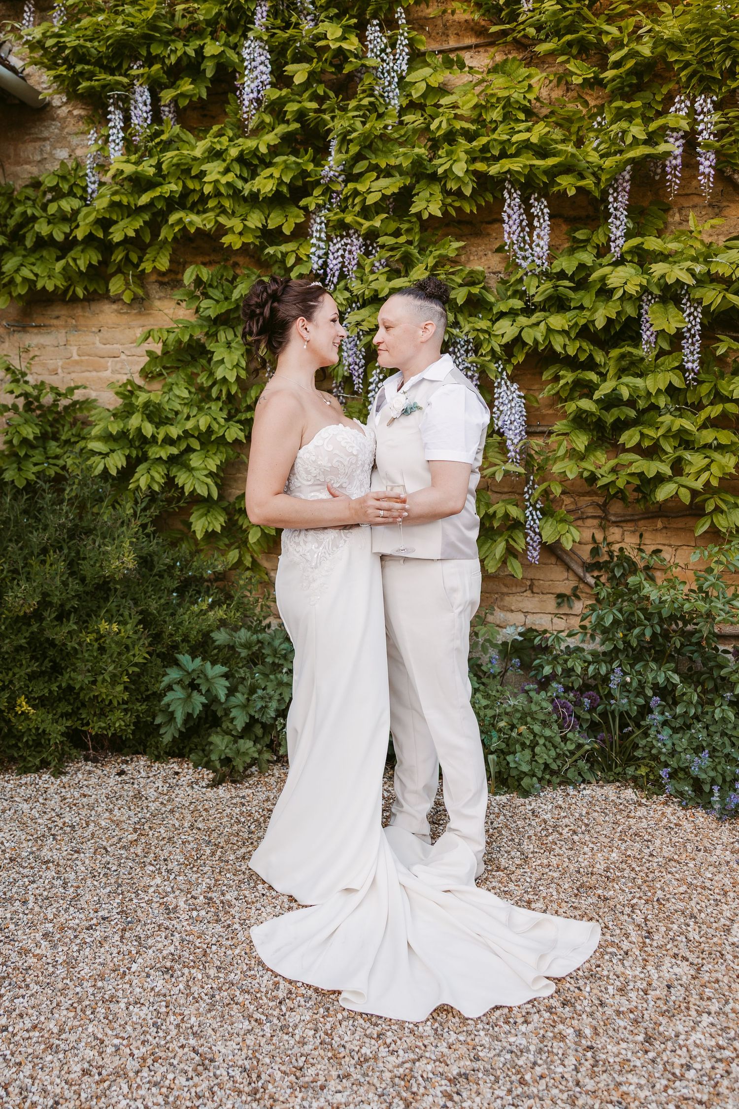 A romantic wedding moment captured in a garden setting with wisteria vines and gravel path.