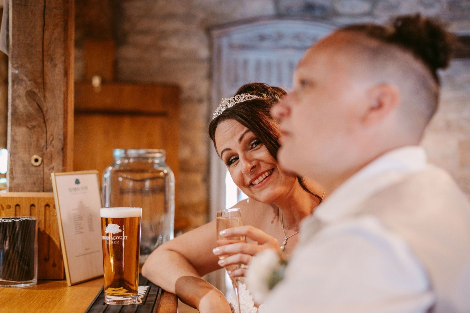 Wedding guests enjoy drinks and conversation at a warmly lit reception venue with rustic wooden details.