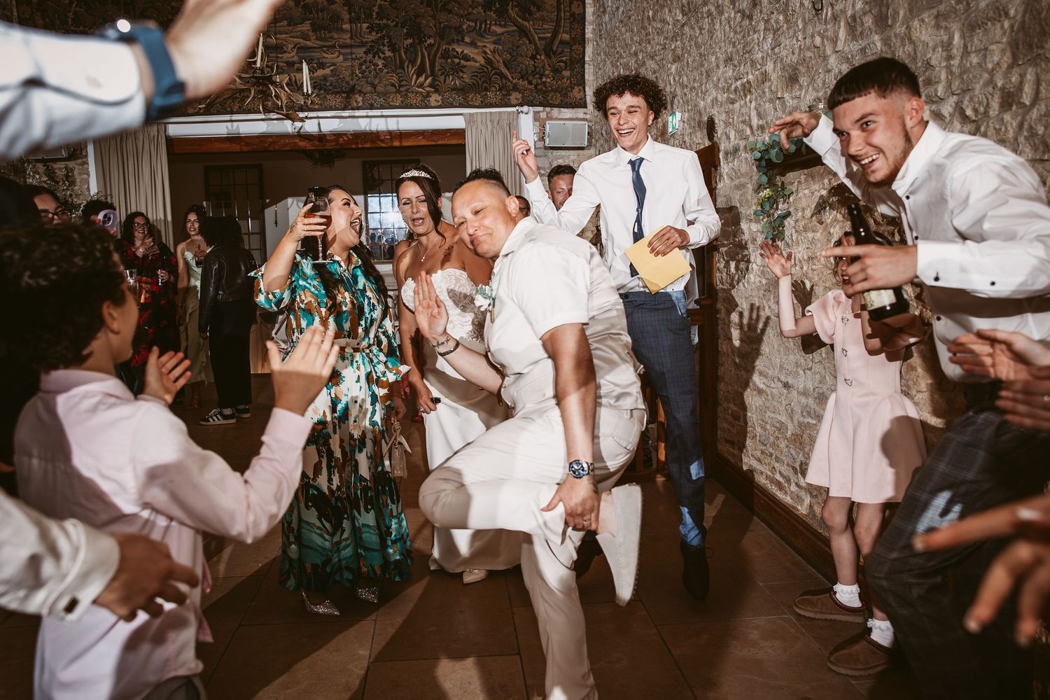 Wedding guests dance joyfully in white outfits during a lively celebration on the dance floor.