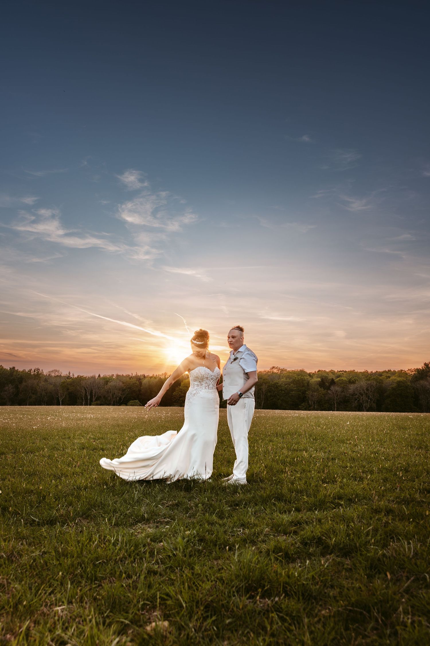 Couple in wedding attire poses in a golden field at sunset creating a romantic silhouette.