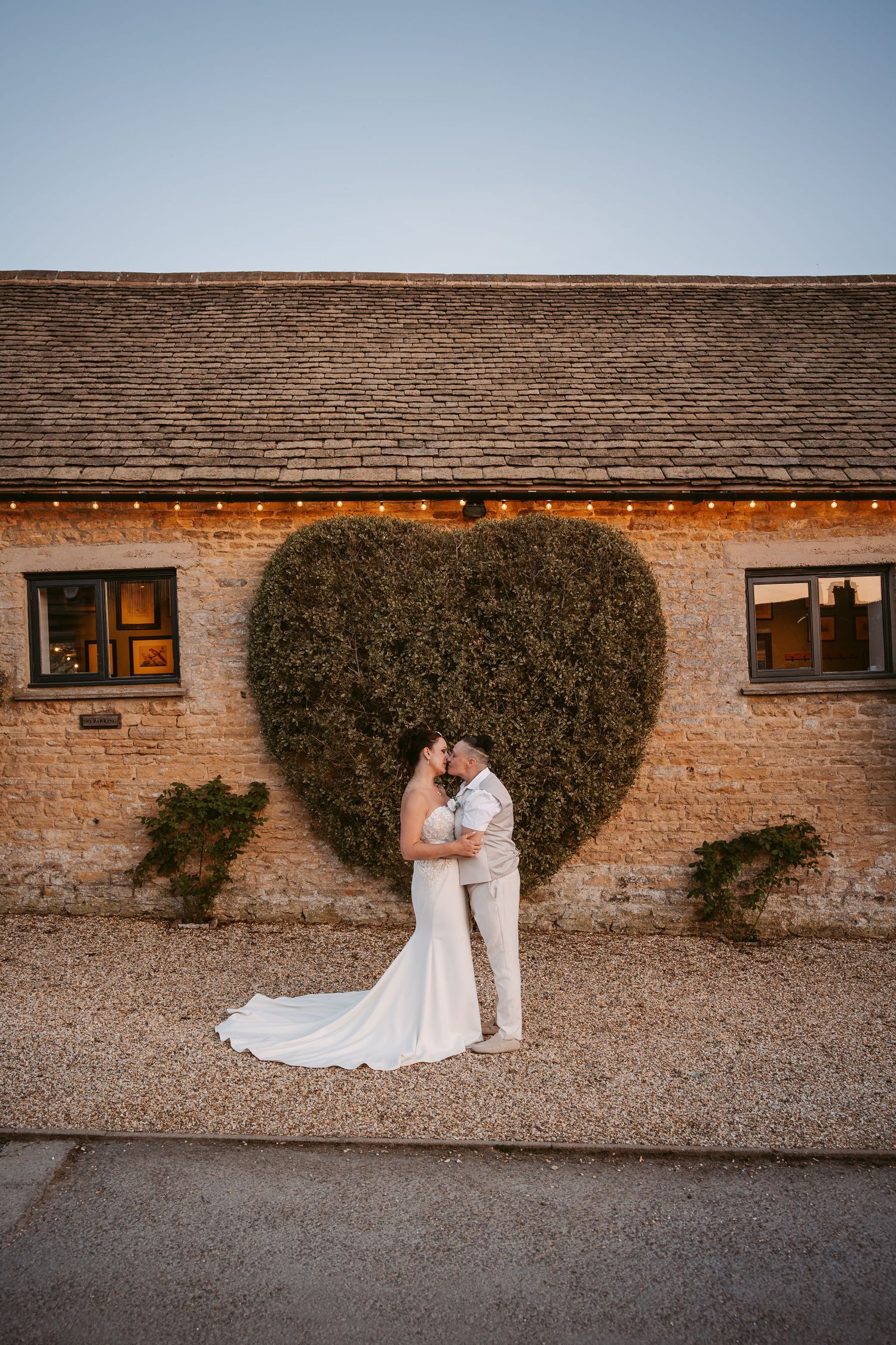 A series of romantic wedding portraits against a rustic brick wall with ivy and string lights at dusk.