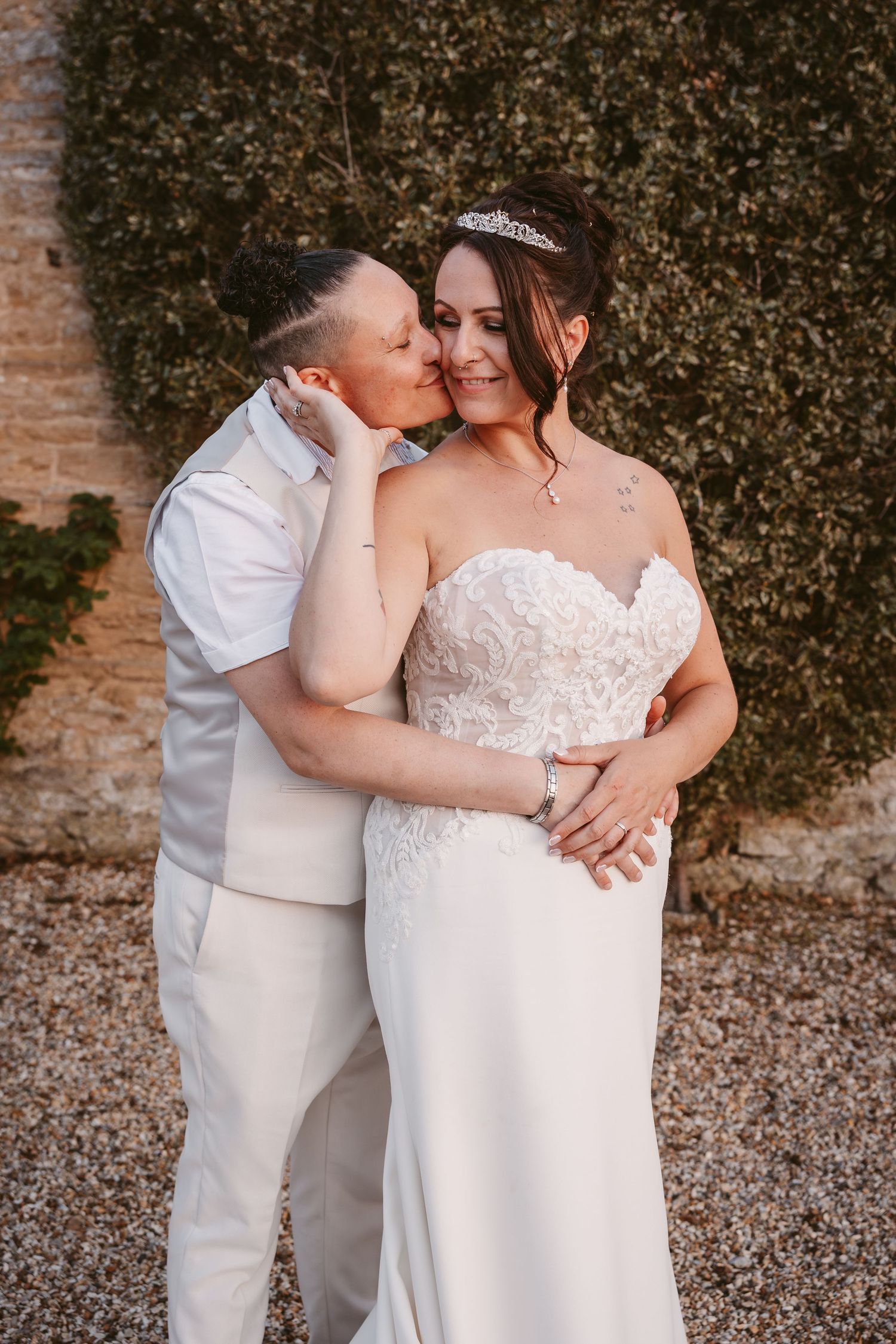 Intimate wedding couple shares tender moments in front of a rustic brick wall and greenery.
