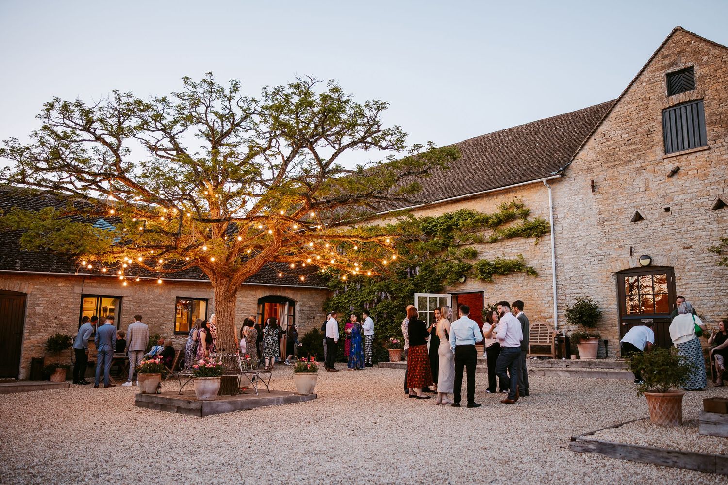 Rustic stone barn wedding venue courtyard with guests mingling during golden hour reception.