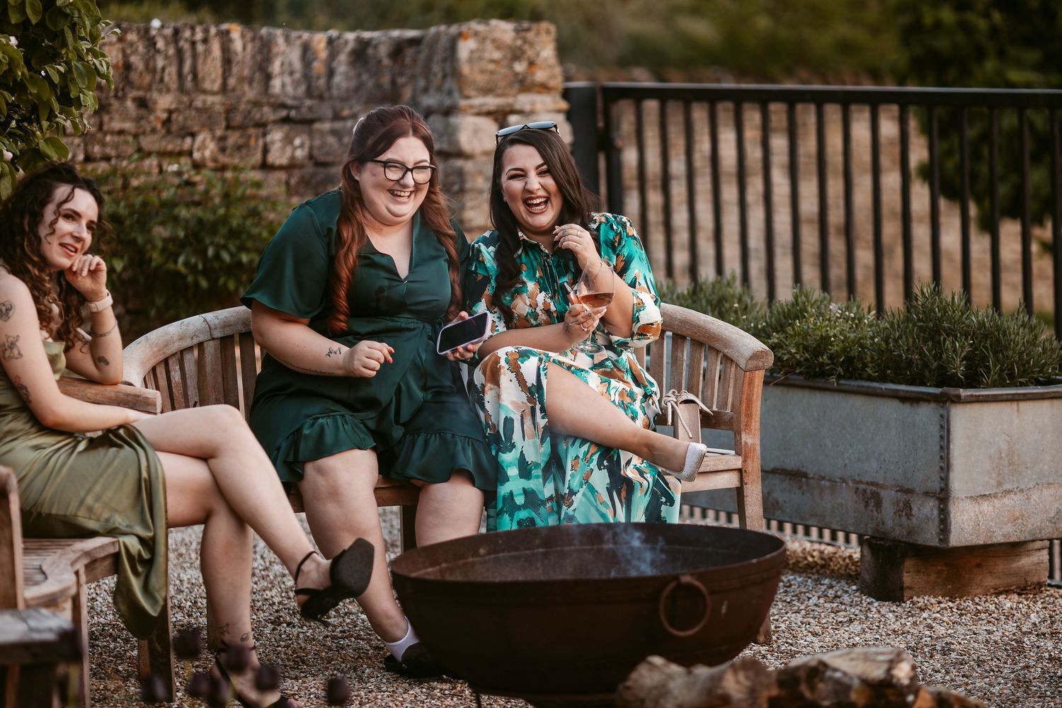 Group enjoying a casual outdoor gathering on rustic wooden benches against a stone wall backdrop.