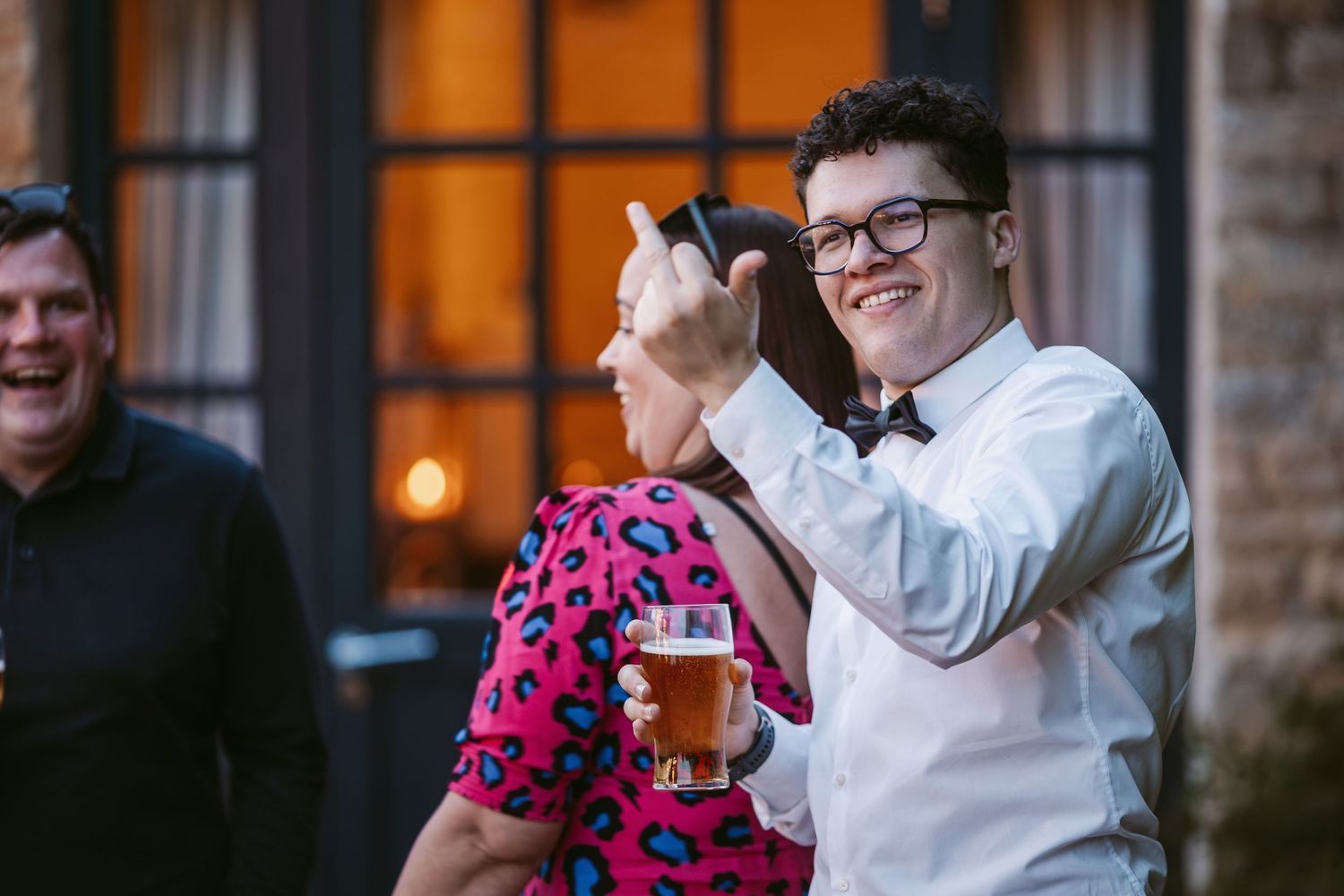 People enjoying drinks and laughter outside a building with warm lighting in the evening.