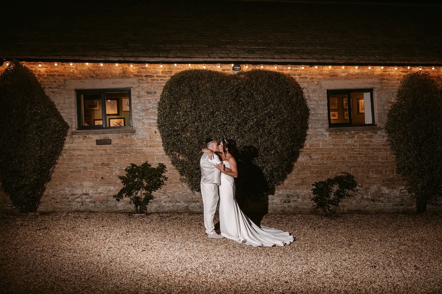 Wedding party poses against rustic brick wall with string lights creating romantic evening ambiance.
