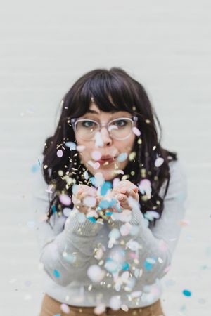 A person wearing glasses blows confetti and colorful paper bits into the air in a playful photo sequence.