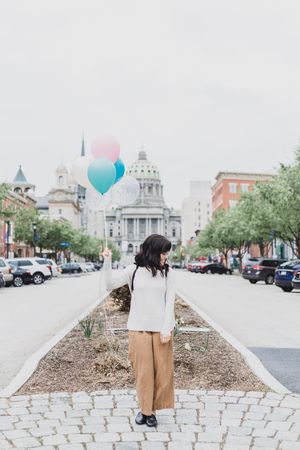 Person walking down cobblestone street with pink and turquoise balloons in urban setting.