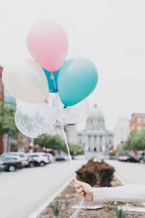Pink and blue balloons float against a cloudy sky in an urban setting with historic architecture in the background.
