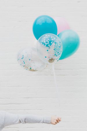 Clear and turquoise balloons with glitter confetti float against a white background in a festive party arrangement.