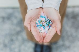 Hands holding small blue and pink confetti pieces against a light gray background.