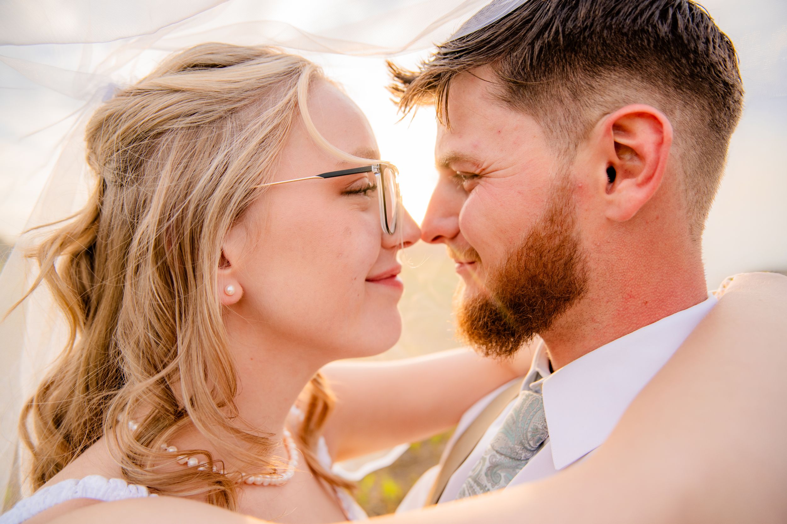 A bride and groom share a romantic close moment under a veil on their wedding day.