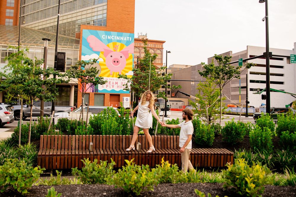 Couple walking on a wooden bench in an urban garden with a colorful Cincinnati mural in the background.